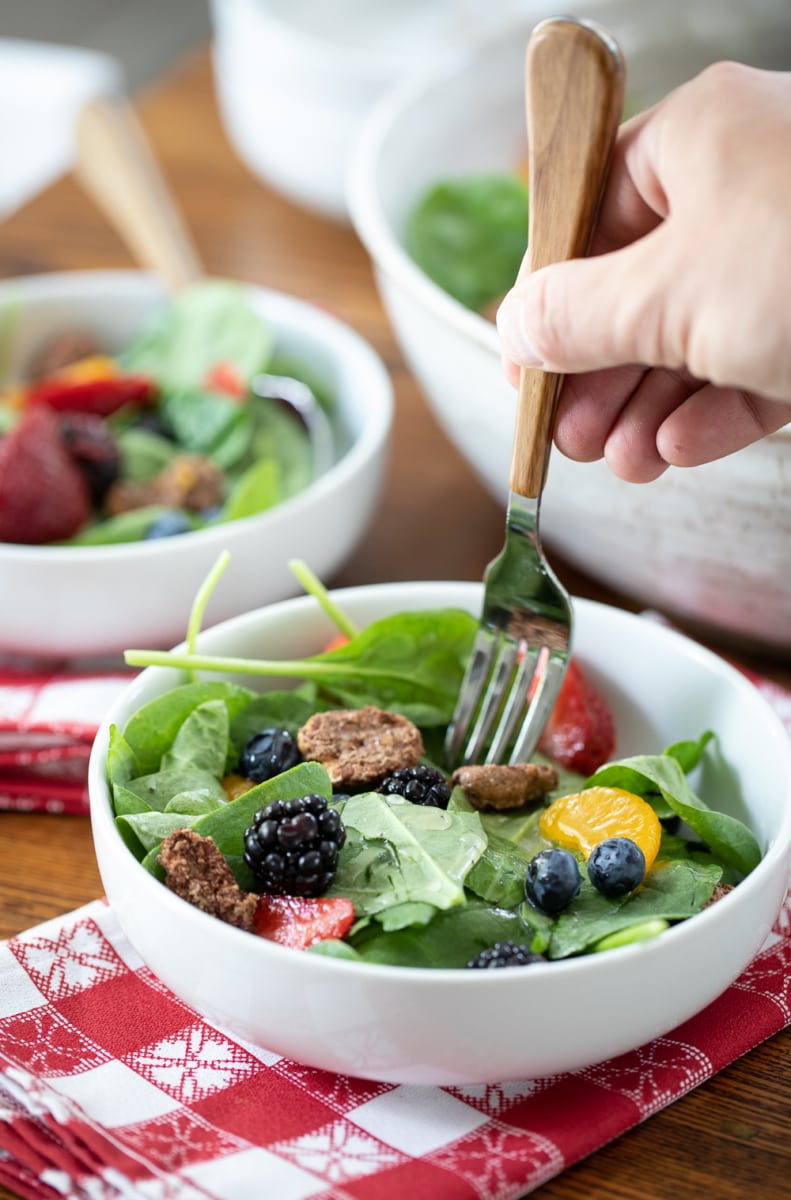 fork into a bowl of spinach salad with berries.