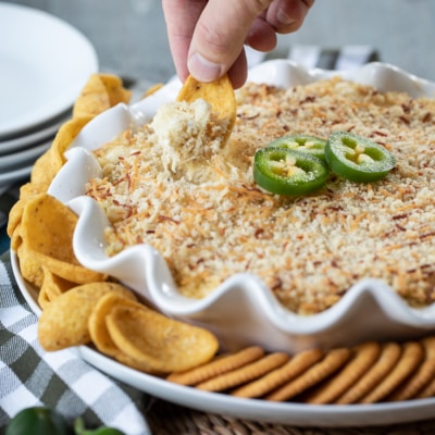 alapeño Popper Dip in dish with hand scooping dip.