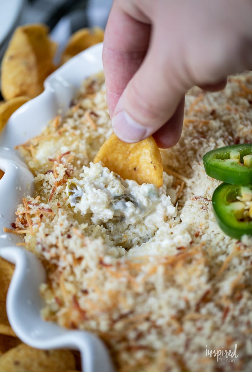 jalapeño Popper Dip in dish with hand scooping dip.