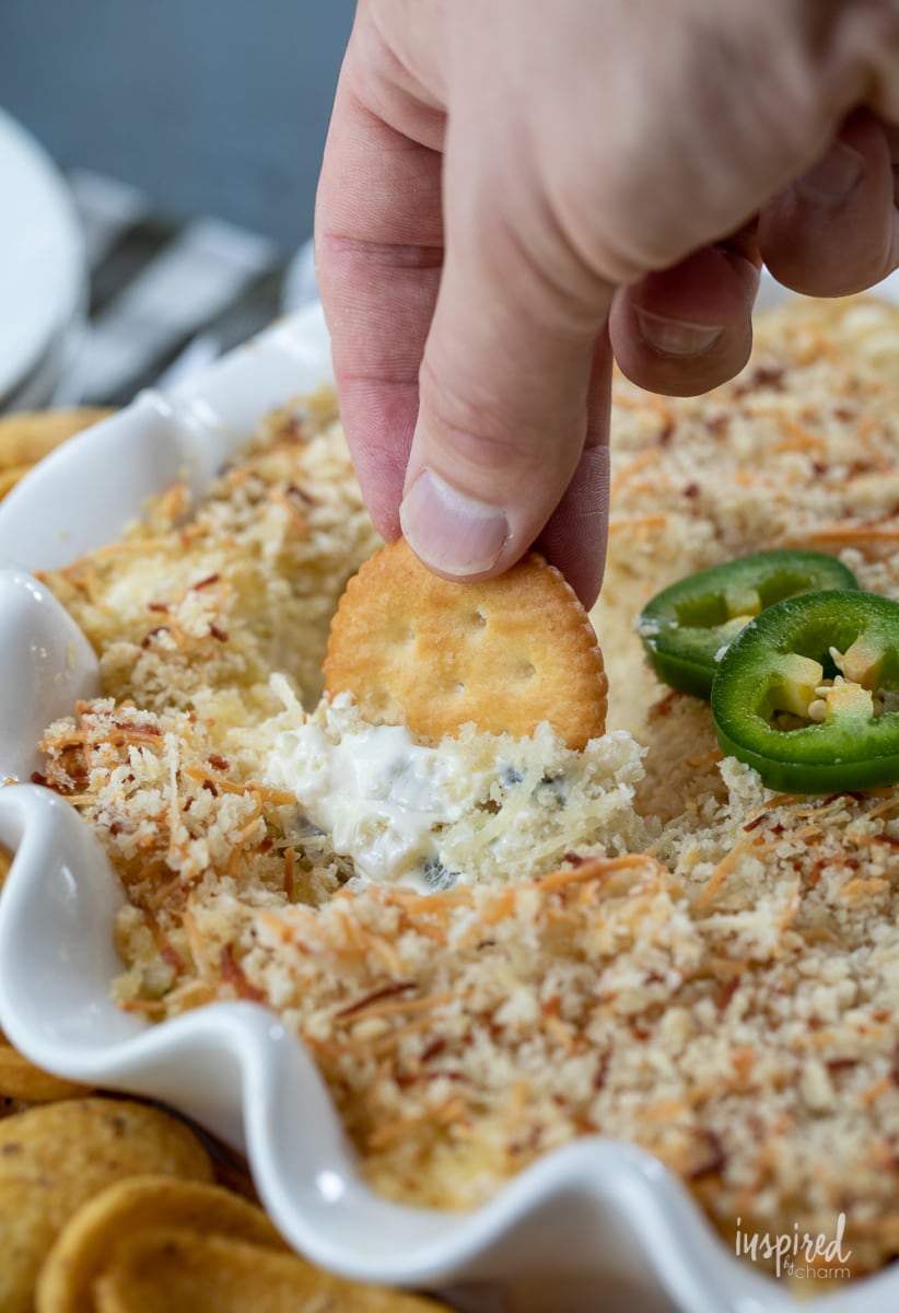 jalapeño Popper Dip in dish with hand scooping dip. 