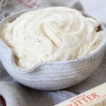 Brown Butter Cream Cheese Frosting in a large bowl with a stick of butter nearby.