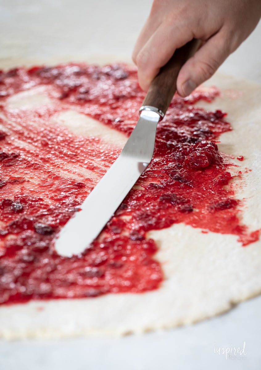 spreading cranberry sauce on dough. 