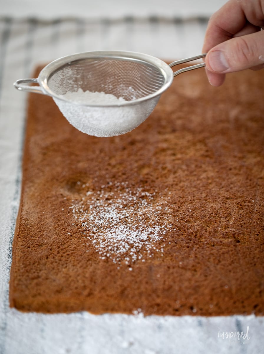 sprinkling confectiners' sugar on a gingerbread swiss cake roll. 