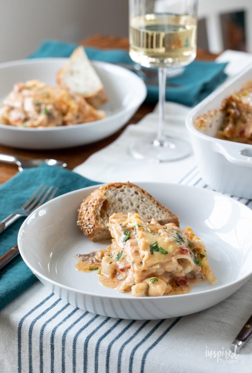 seafood lasagna on plate with bread and wine.