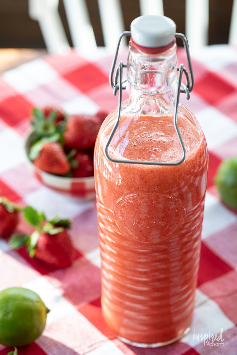 Homemade Strawberry Margarita mix in a bottle with strawberries and limes.