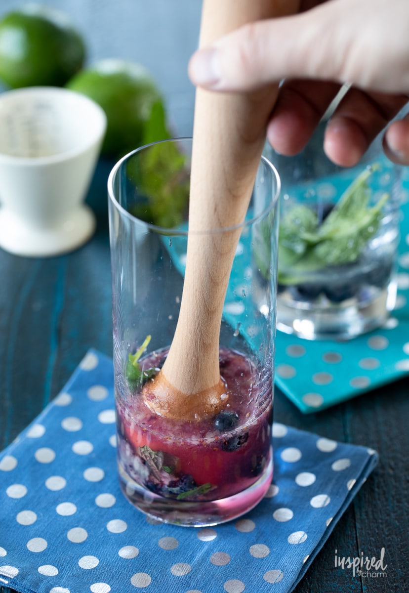 hand muddling blueberries and mint for mojito.