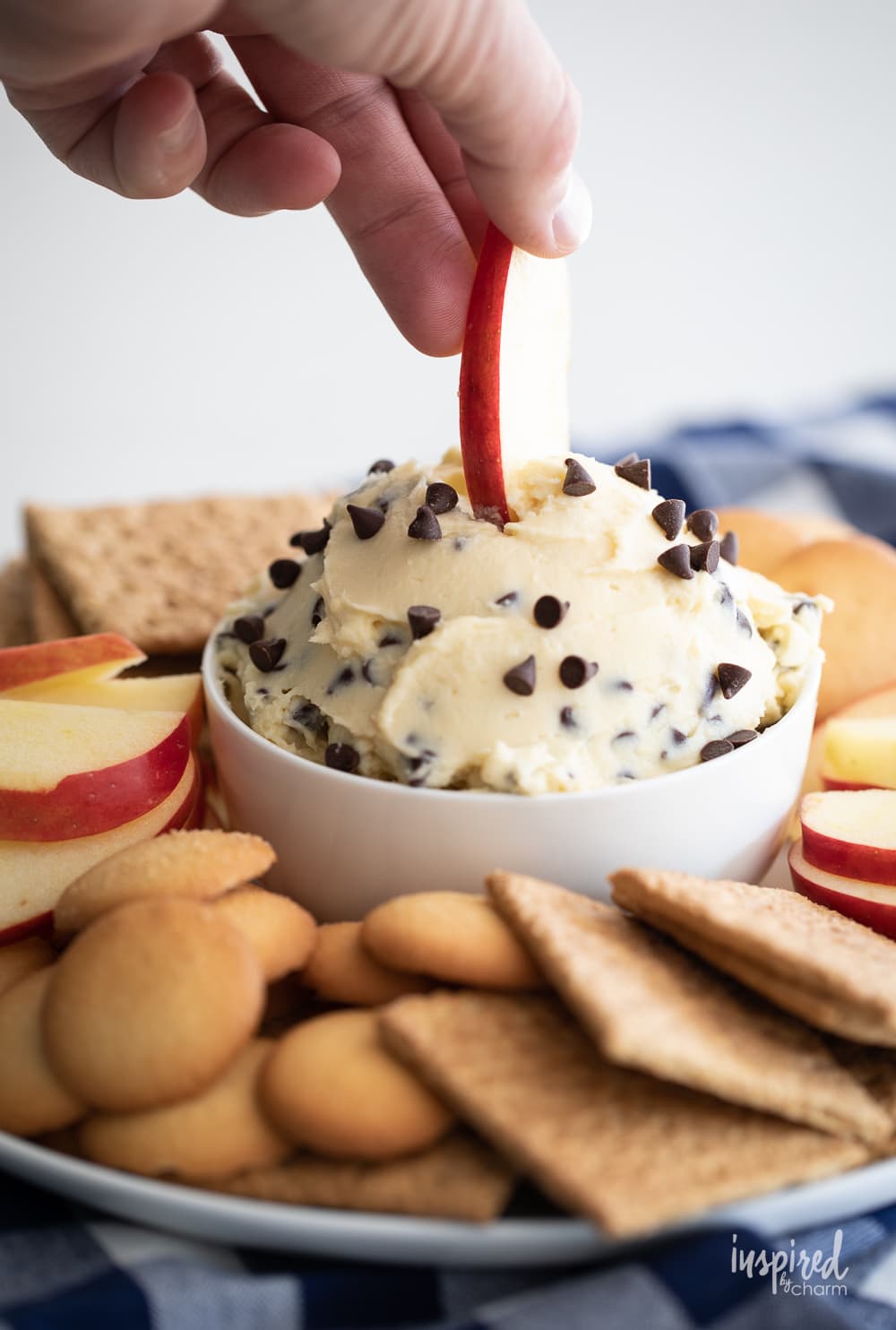 hand dipping apple slice into chocolate chip cheesecake dip.