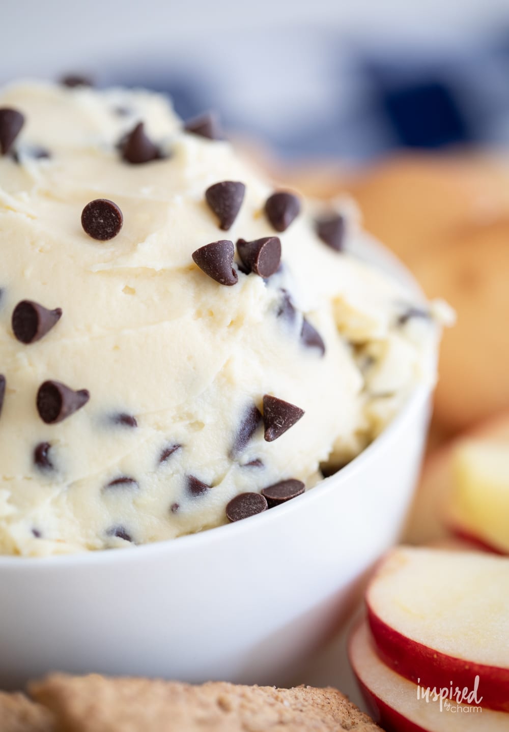 up close chocolate chip cheesecake dip in a bowl with cookies and apple slices.