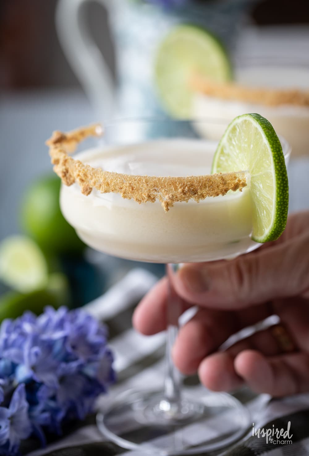 hand holding key lime pie martini in a glass with a lime garnish.