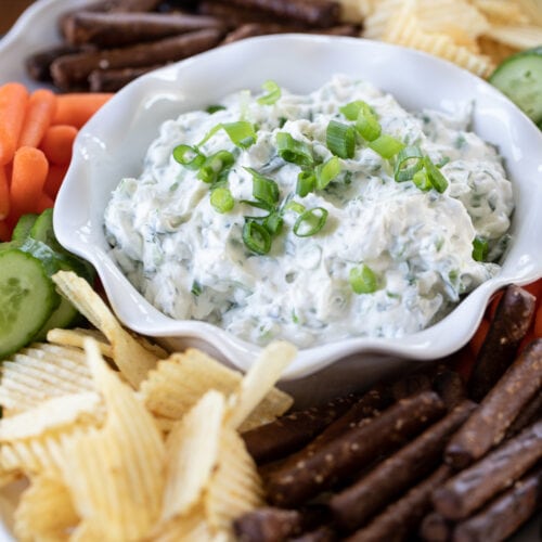 green onion dip in a bowl on a plate with chips and vegetables.