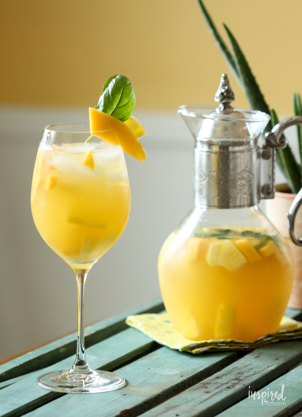 pineapple mango sangria in a glass with mango and basil garnish with pitcher of sangria. 