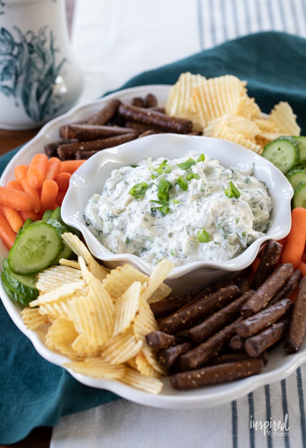green onion dip in a bowl on a plate with chips and vegetables.