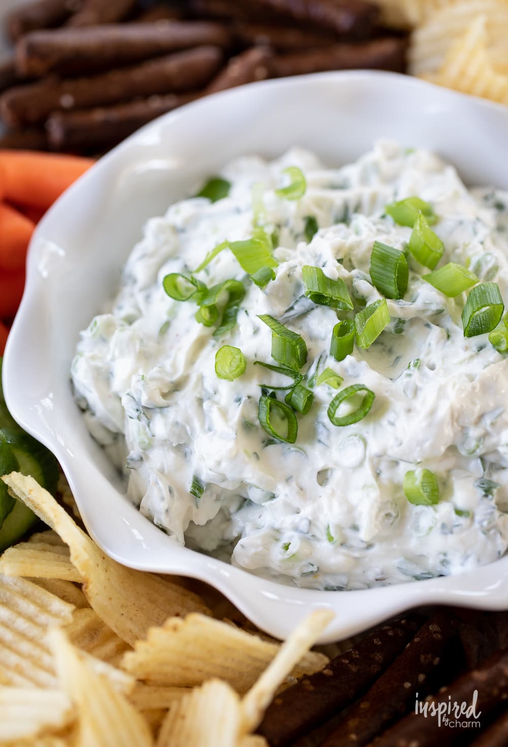 close up of green onion dip in a bowl on a plate with chips and vegetables.