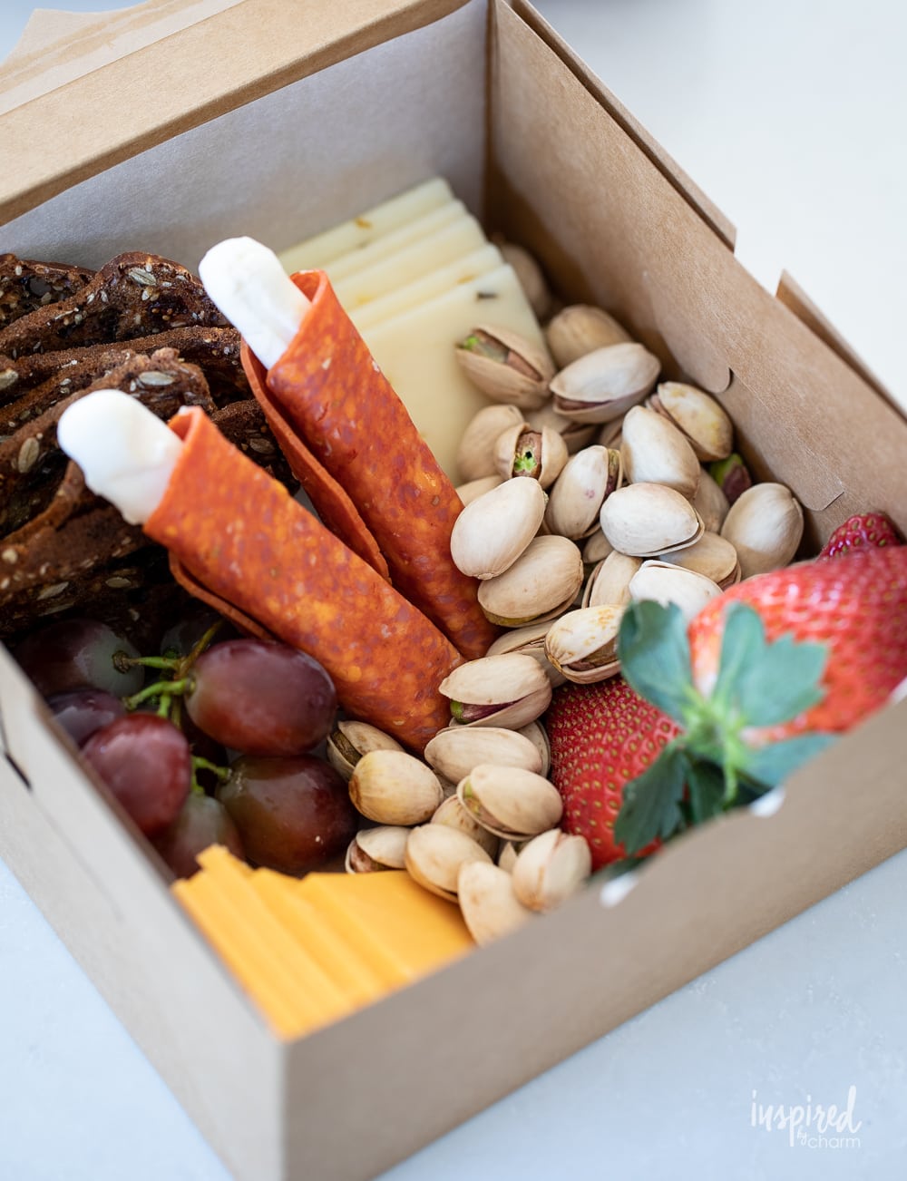 filling a charcuterie box with meats, cheeses, and nuts.