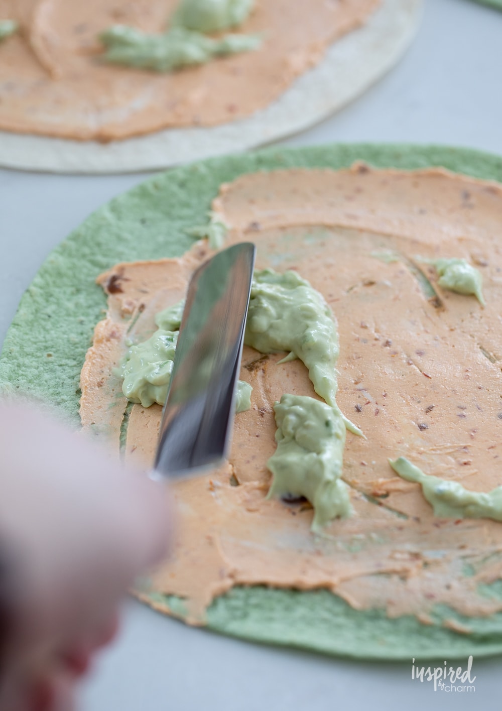 cream cheese and avocado mayo spread being spread onto a flour tortilla. 