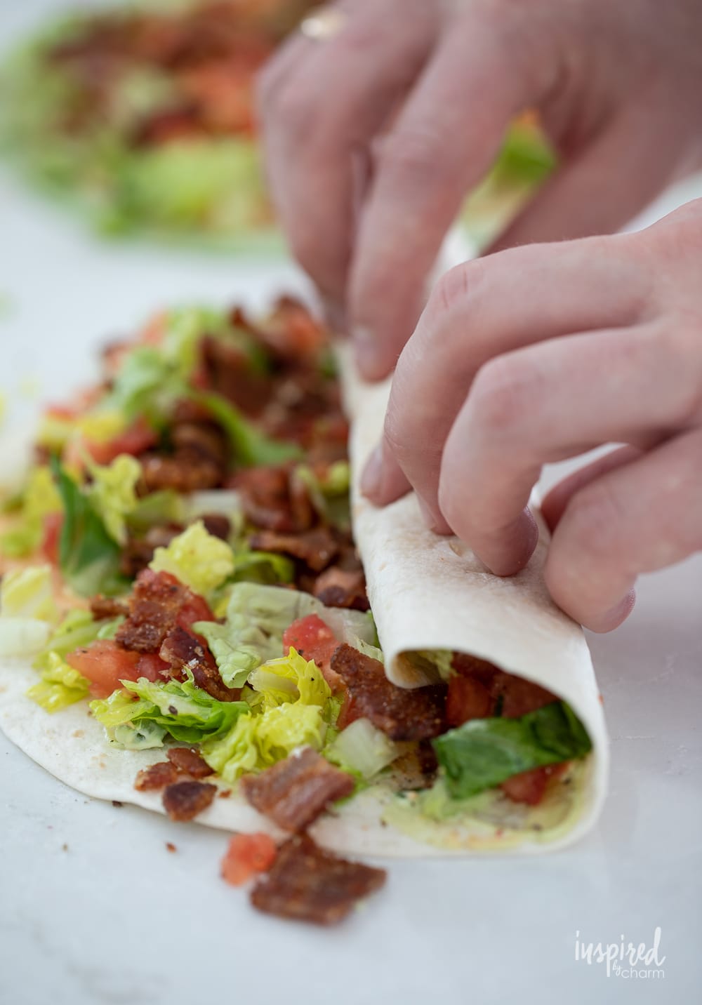 two hands rolling up a flour tortilla to make BLT Pinwheel Sandwiches.