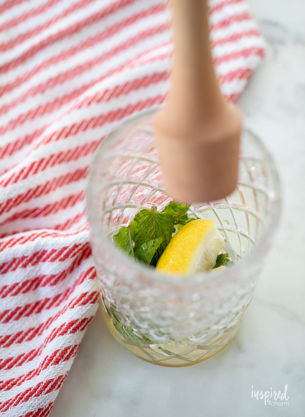 muddler in cocktail shaker with mint and lemon.