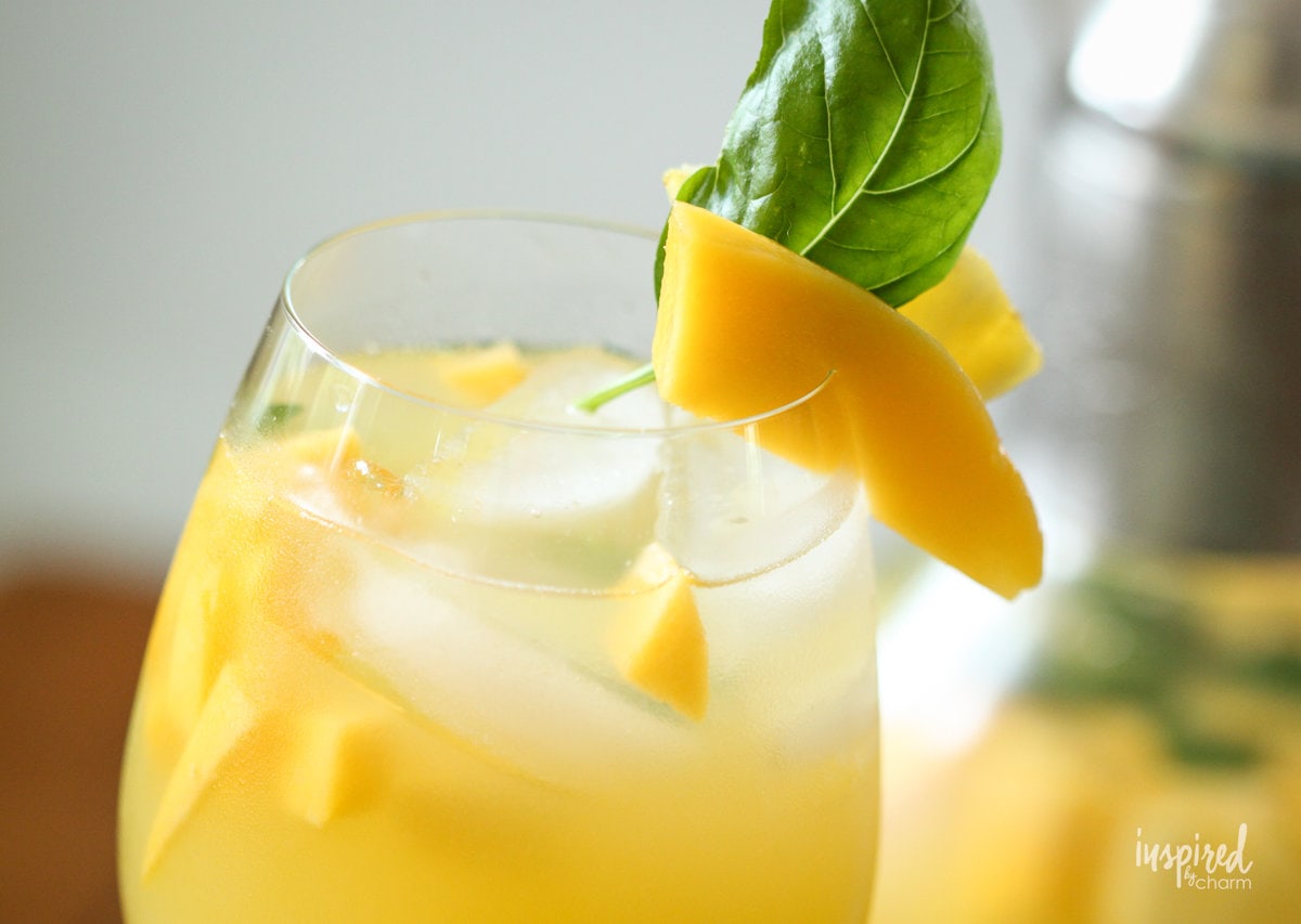 pineapple mango sangria in a glass with mango and basil garnish. 