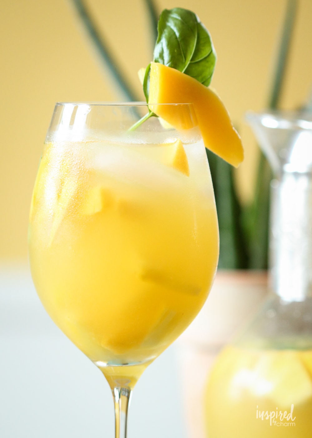 up close pineapple mango sangria in a glass with mango and basil garnish. 