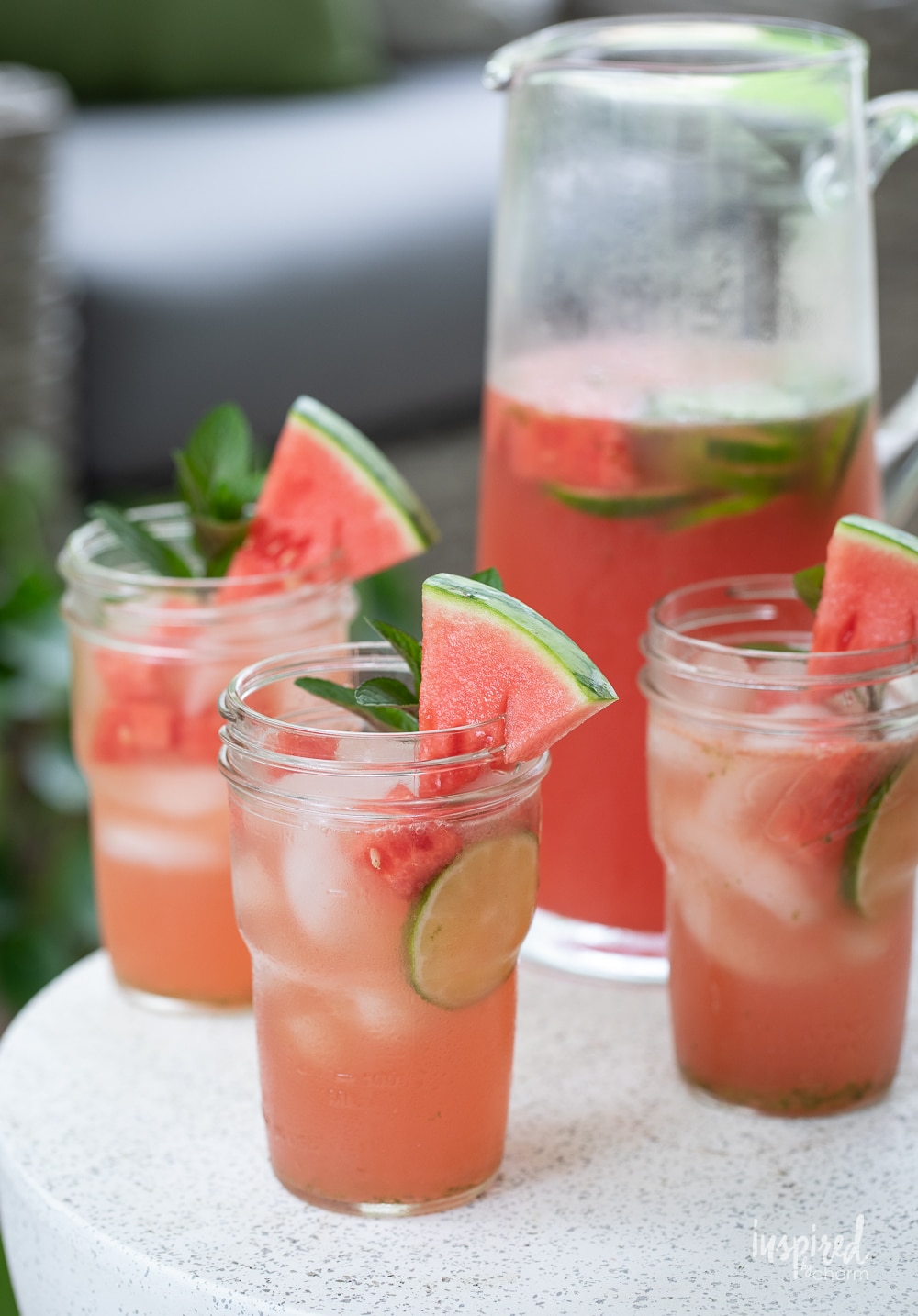 three glasses of watermelon sangria with a pitcher of sangria behind them.