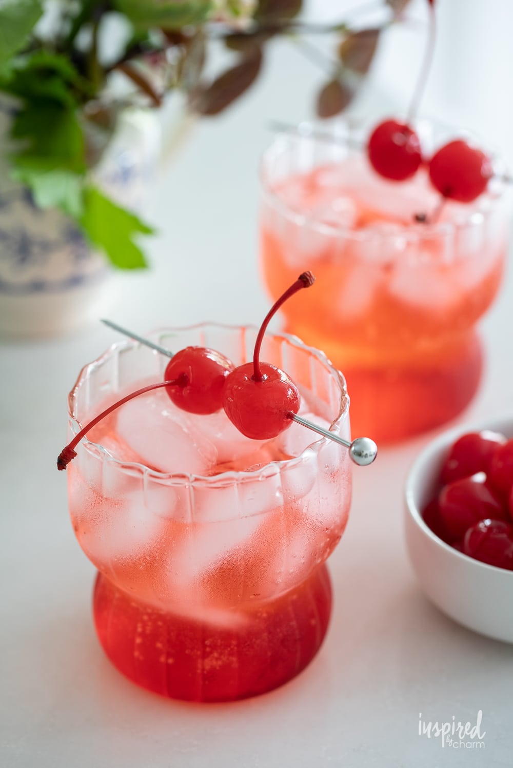 two dirty shirley drinks in glass with a maraschino cherry garnish.