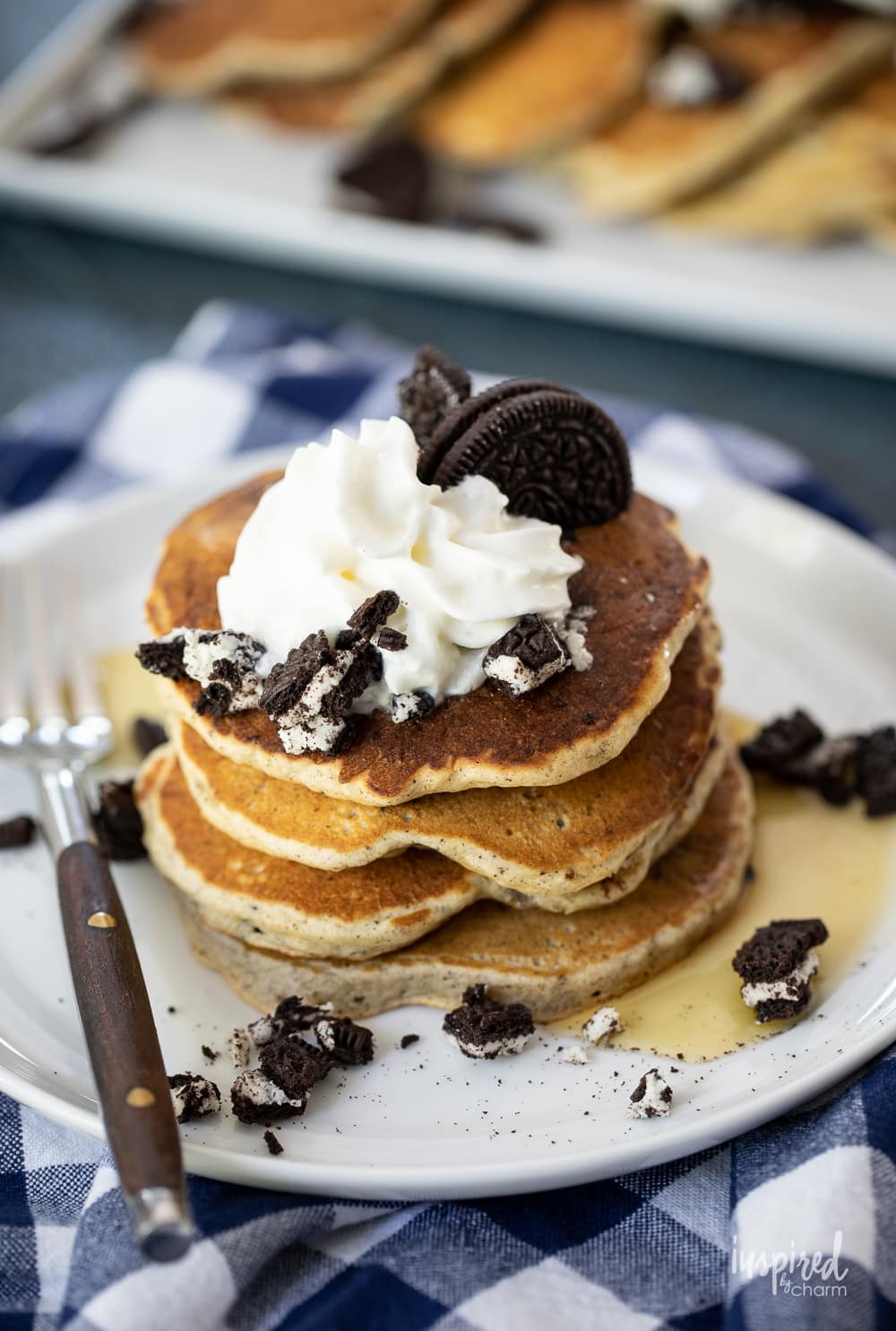 stack of Oreo pancakes on a plate with whipped cream and syrup.
