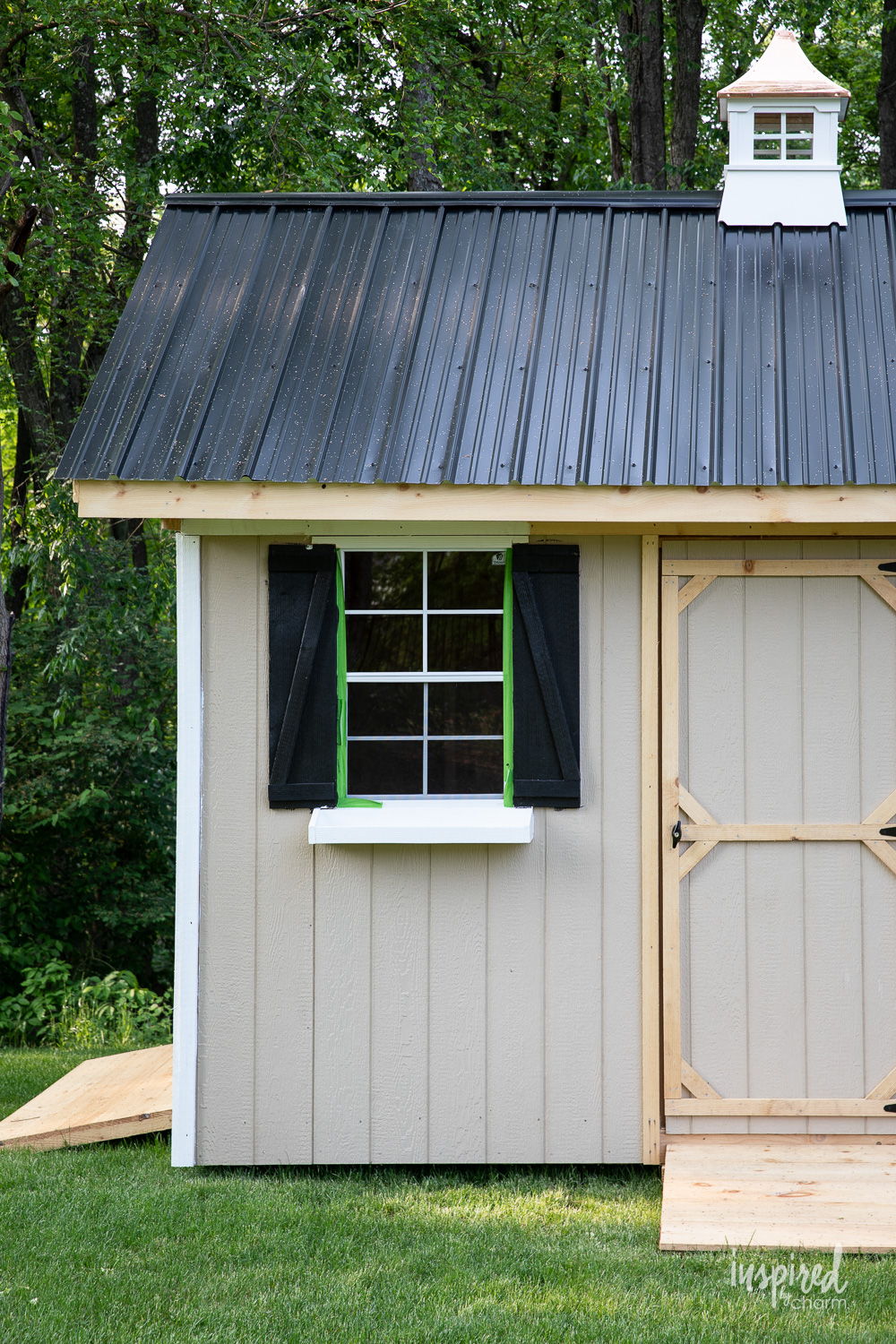 tan shed with black shutters and roof with white trim.