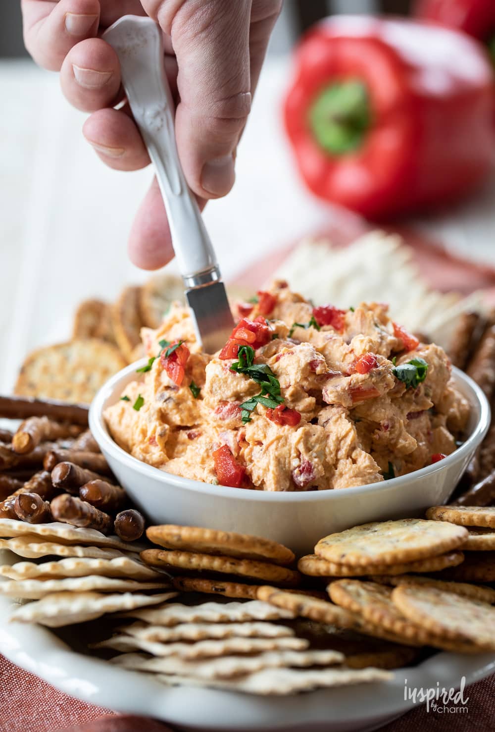 hand serving roasted red pepper dip in a bowl.