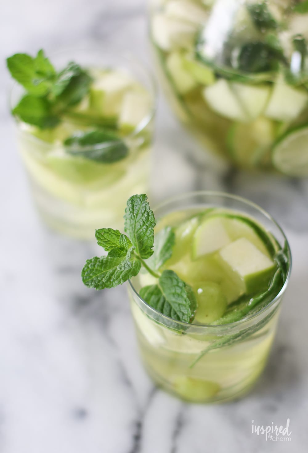 sangria verde in two glasses garnished with apples, mint and grapes