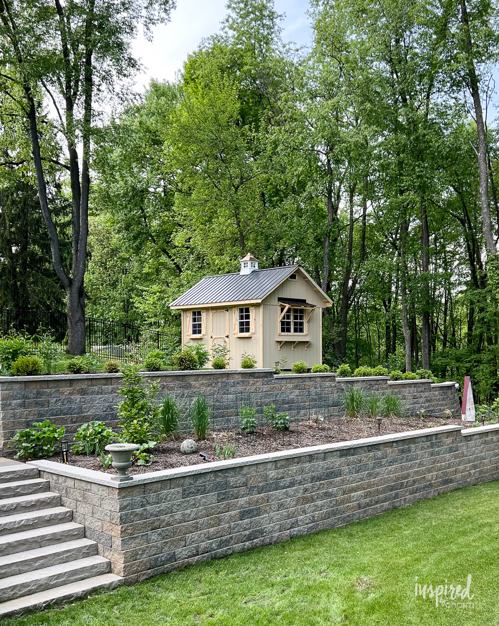 wood shed in a backyard on top of a retaining wall of stone.