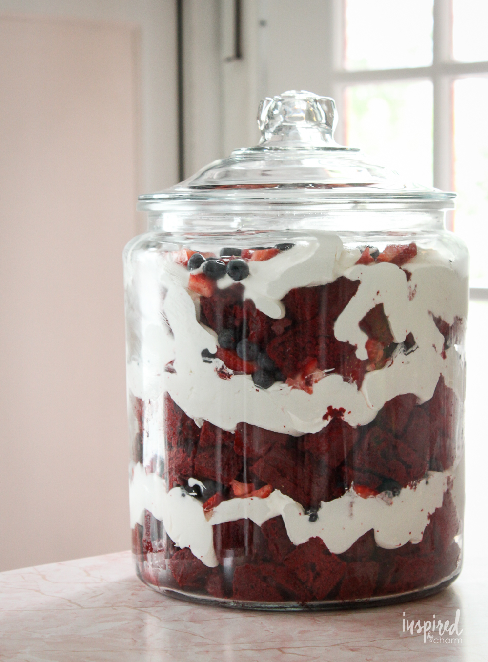 red velvet trifle layered with berries and whipped cream in a large glass jar.