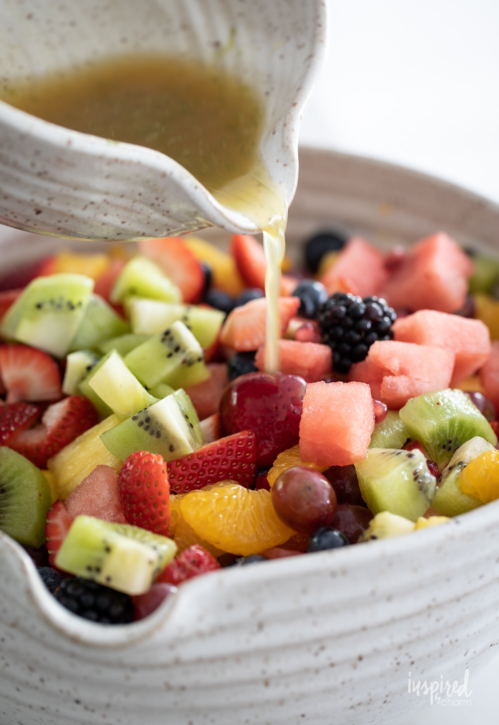 pouring dressing over a big bowl of colorful fruit salad.