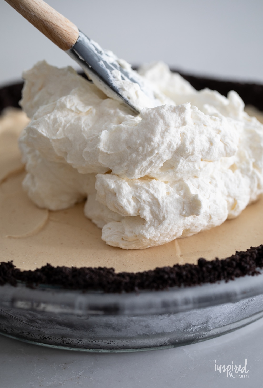 adding whipped cream to the top of a peanut butter ice cream pie.