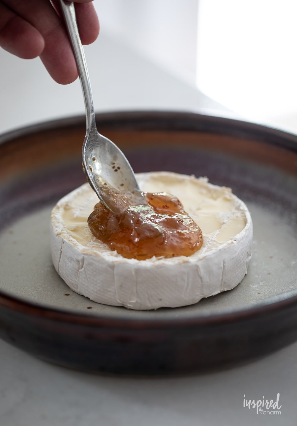 spooning fig jam on the top of a wheel of brie cheese in a pan. 