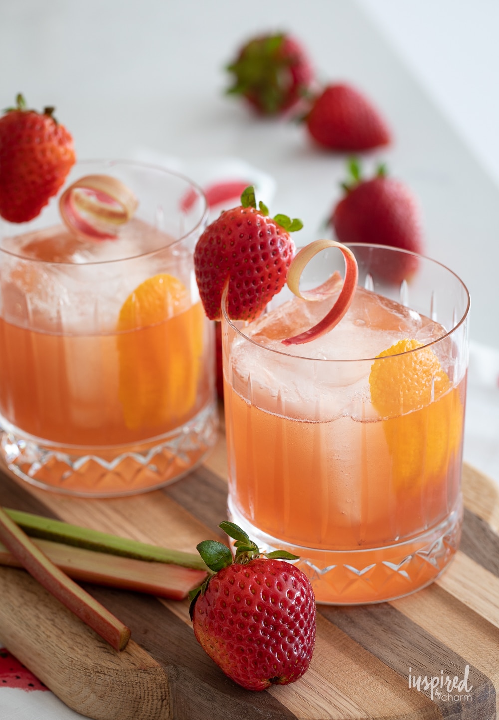 strawberry rhubarb old fashioned in glasses with strawberry and rhubarb garnish.