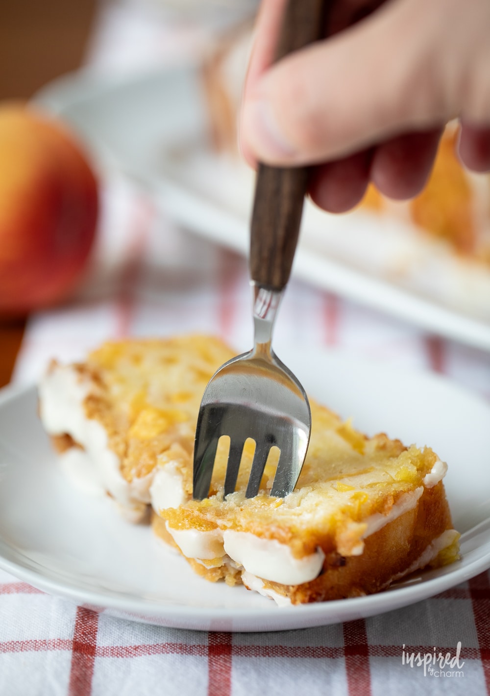 hand with a fork taking a bite of peach cobbler pound cake on a plate.