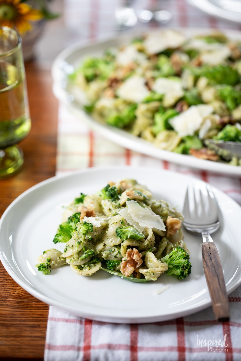 serving of broccoli pasta salad on a plate with a platter of more in the background. 