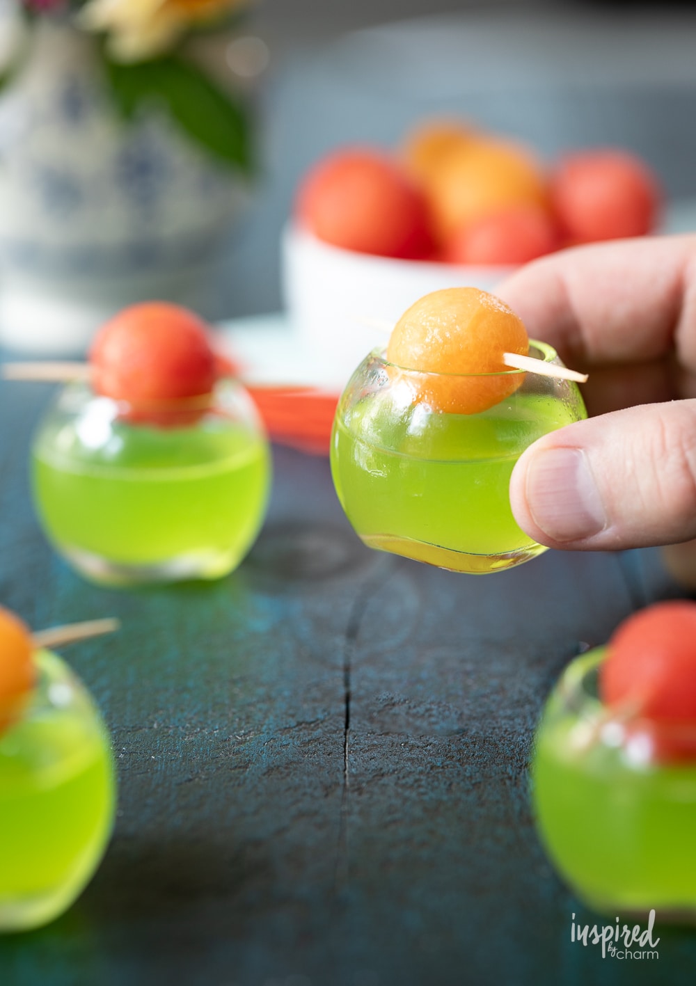 hand holding a melon ball shot in a small round glass.