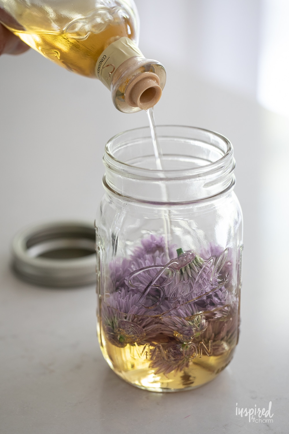 pouring white balsamic vinegar into jar with chive blossoms.
