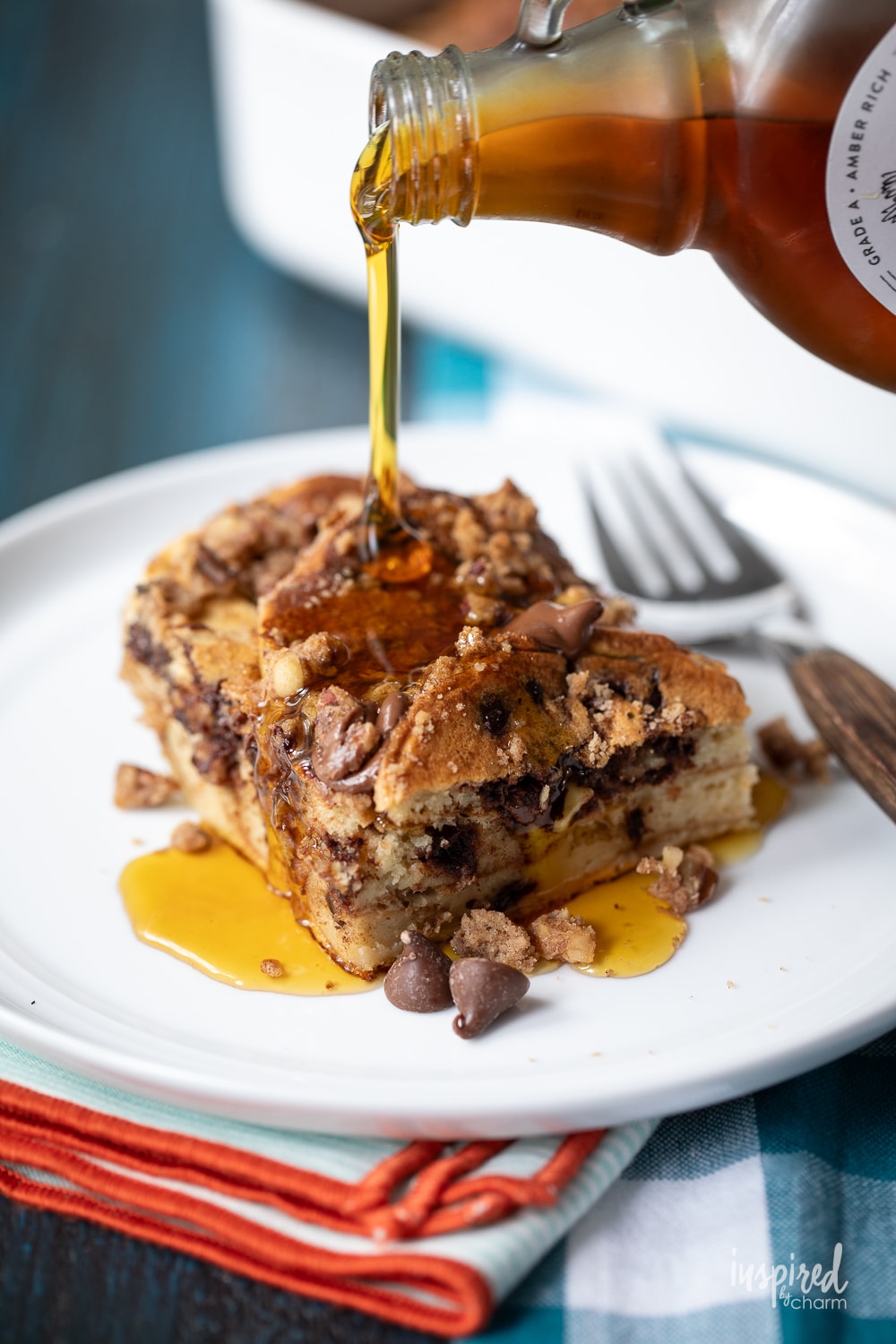 pouring maple syrup on a piece of chocolate chip pancake casserole on a white plate.