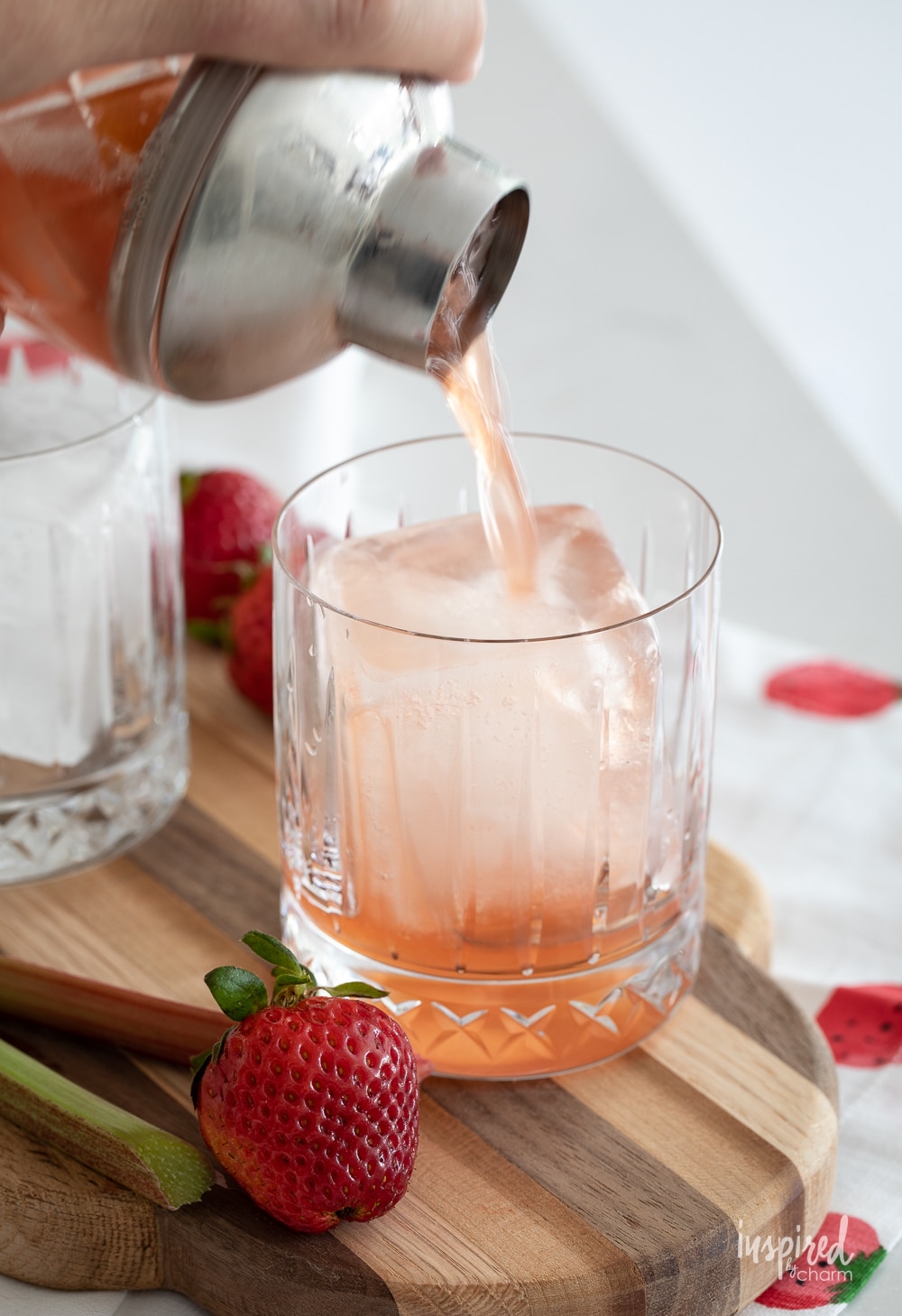 pouring a strawberry rhubarb old fashioned into a rocks glass with large ice cube.
