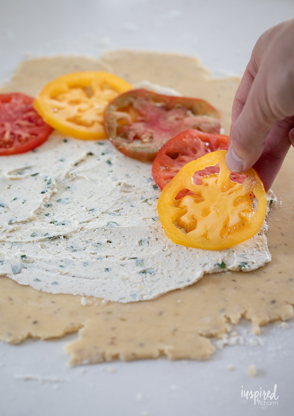 adding tomato slices to a rolled out crust with goat cheese.