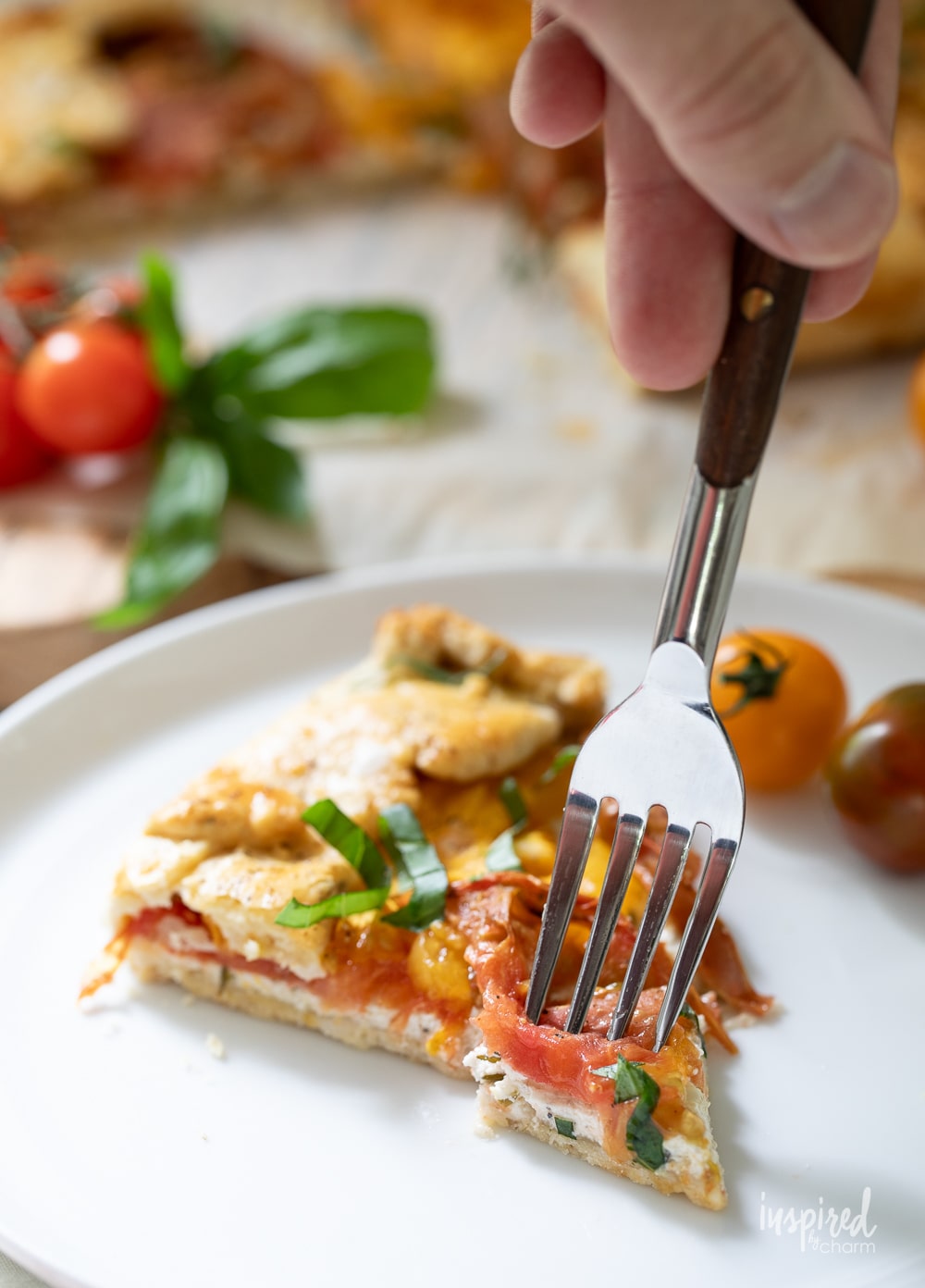 hand with fork into a slice of tomato galette.