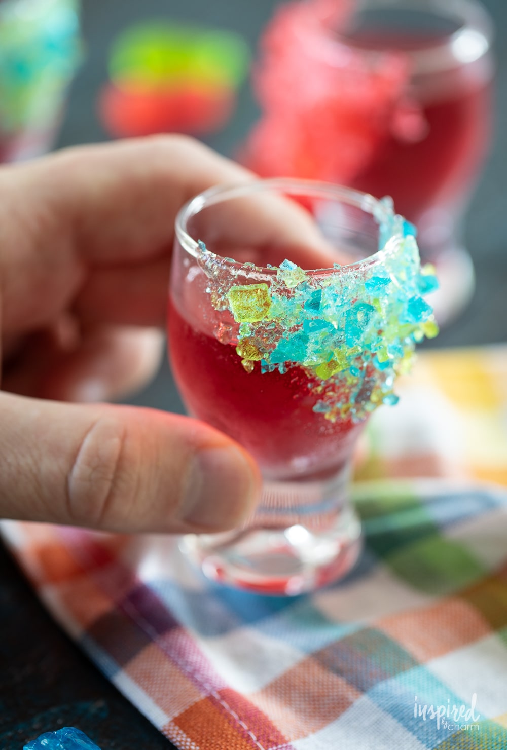 hand holding shot glass with jolly rancher drink and crushed candy garnish.