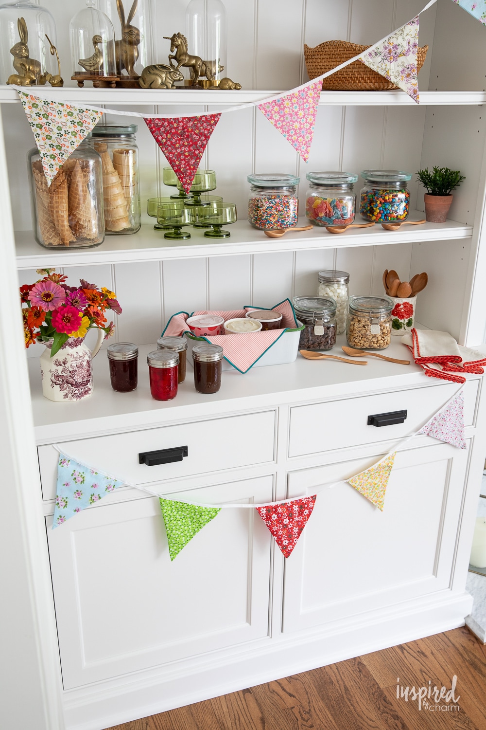 colorful ice cream sundae bar with toppings and cones in glass jars and a colorful pendant garland.