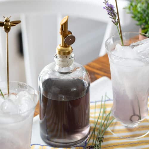 bottle of lavender simple syrup next to glasses of lavender lemonade.