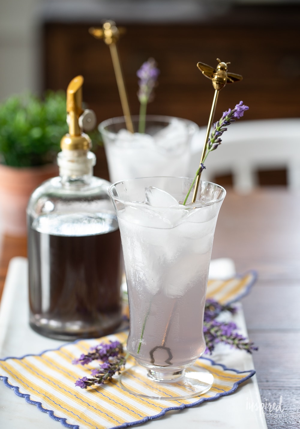 lavender simple syrup set behind a lavender lemonade drink in a glass.