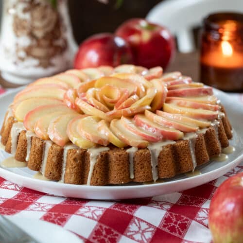 fresh apple cake arranged on a table with flowers, candle, and fresh apples.