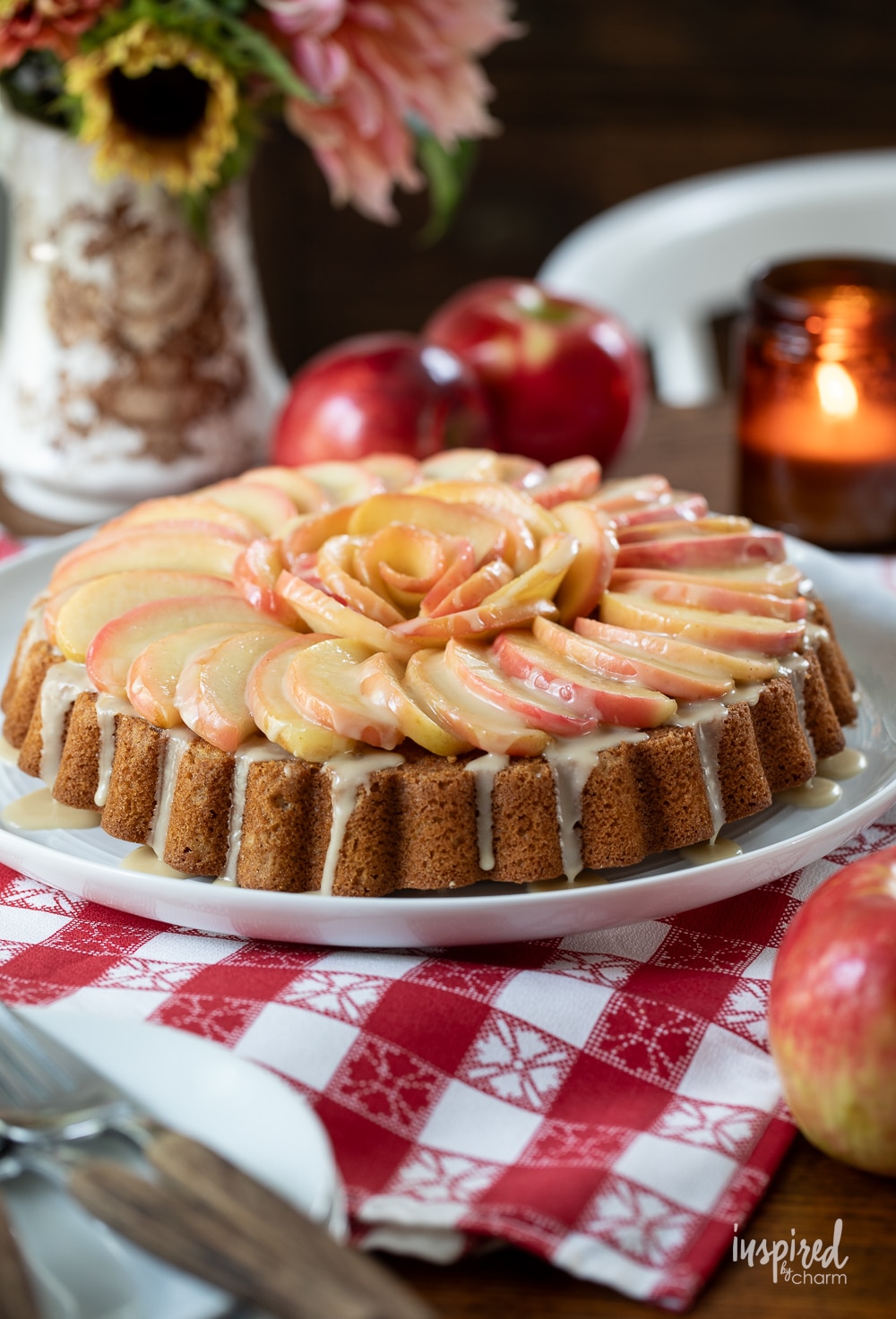 fresh apple cake arranged on a table with flowers, candle, and fresh apples.