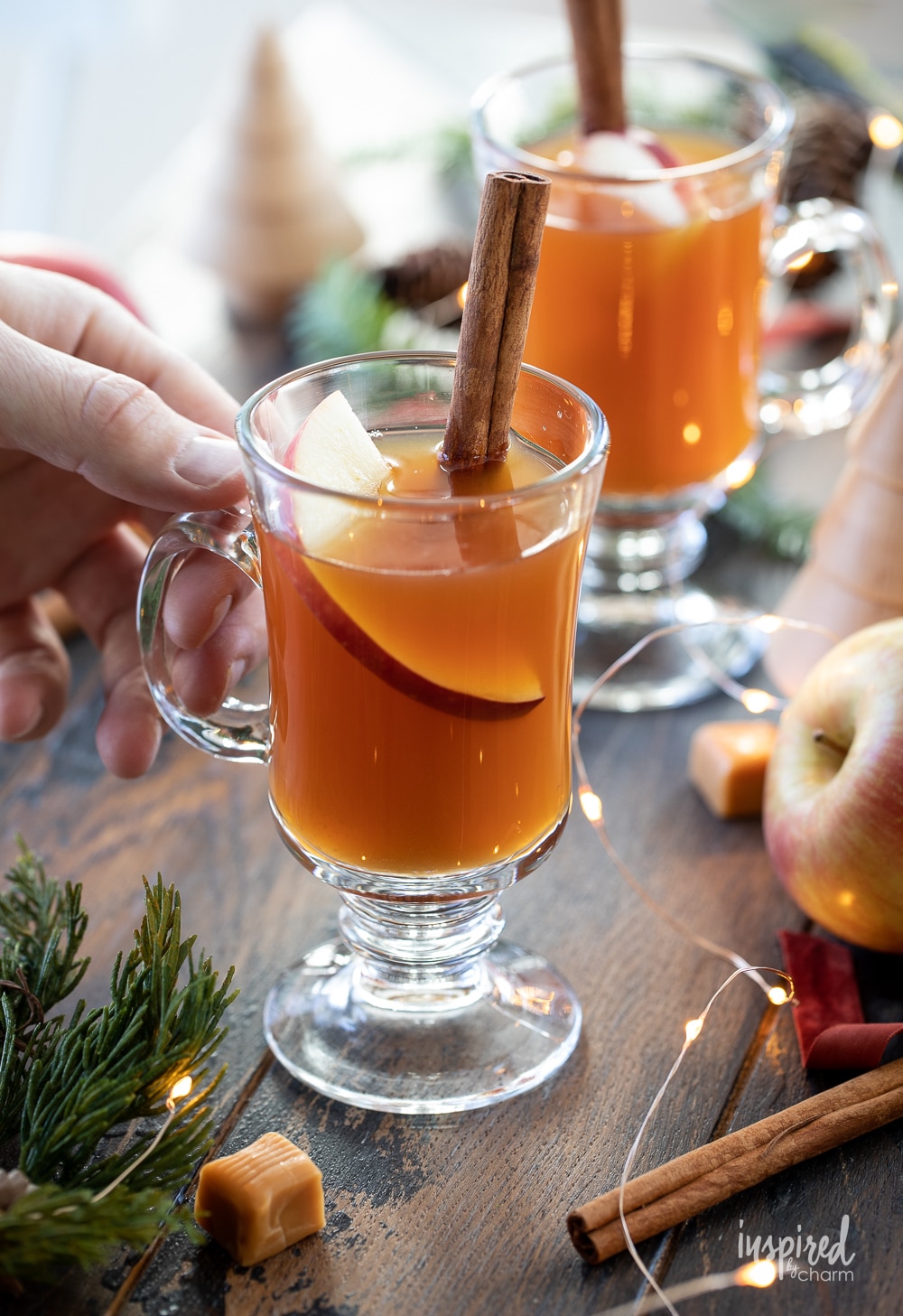 hand holding a glass mug of caramel apple cider tea cocktail. 